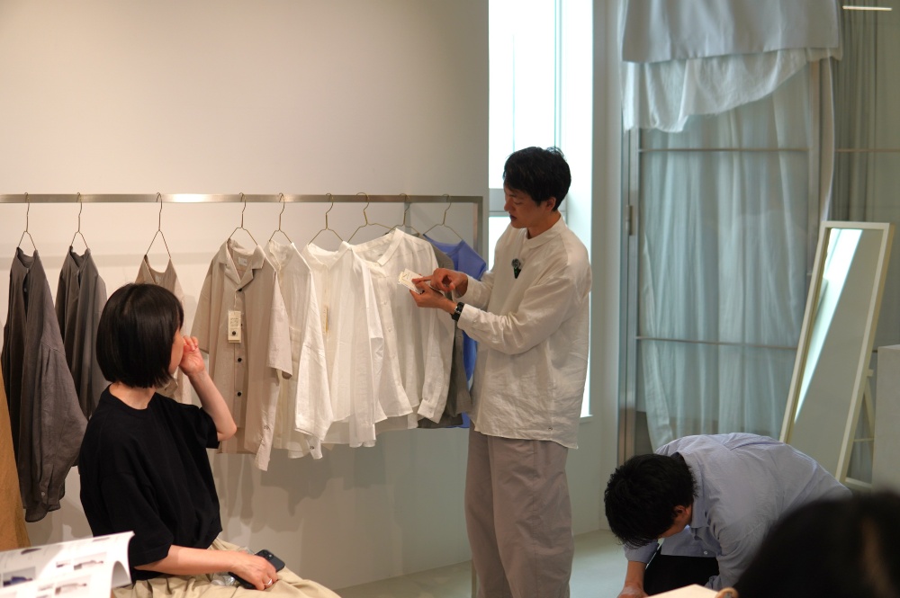 他産地の倍以上の糸を贅沢に使用し、時間をかけて高密度に織り上げる遠州織物。どうしても生産量は限られ、価格も一般的な服より高価になります。“日々の暮らしの中に馴染む上質な日常着”をコンセプトに掲げるHUISは、遠州の技術が生み出す最高品質の生地を、特別な日だけでなく日常の中で使ってもらうことを目指しています。そのために産地内に拠点を置き、生地の企画から参加。織屋さんとの信頼関係をもとに直接生地を仕入れることで、可能な限り価格を抑える努力を続けています。それでも松下さんは「“地元で作っている”という理由だけでは、なかなか2万円を超える服を買っていただけない」と言います。「HUISにとって最も大切なのは、売り場での接客コミュニケーションを通じて価値を伝えること。遠州織物の凄みや、産地のこんなに楽しい背景を言葉で伝えていくことにこそ意味があるんです」。実際、全国の百貨店やギャラリーで開催される期間限定POP UPでは、触れた瞬間に違いが分かる生地と、その背景を情熱的に語るスタッフの姿が多くのファンを魅了しています。リアルな場での感動体験がきっかけとなり、その後ECサイトでも購入してもらえるという好循環が生まれました。現在では、全国7箇所にショップインショップ型のショールームを展開しています。