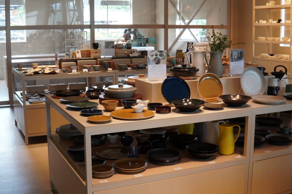 地元商社に商品を卸すのが当たり前だった時代、光洋陶器さんは自社で販売部門を持ち、直接小売店や消費者に販売する道を模索し始めました。当初は産地内で反発を受けることもありましたが、その先見の明が実を結んでいます。現在では製造するだけでなく、一般の方に向けた工場見学を積極的に行い、産地の伝統と技術に触れる機会を通して、モノづくりの魅力を多くの人に届けています。また、本社工場にはかつては出荷場だった倉庫を改装し直営のショップとカフェを併設。ただ工場見学をするだけでなく、「見学した後に、自社で作ったお皿に盛られた料理を実際に食べてもらう」という体験を通じ「土から食卓まで」のストーリーを提供しています。こうした取り組みにより国内はもちろん、海外からの評価も高まっている同社のブランド力を象徴する場所となっていました。